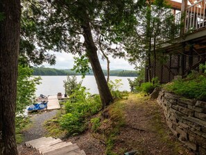 A lakeside property with a dock, a stone wall, and a wooden deck overlooking the water. - La Baie la Vida,Bord de L`eau,Spa et foyer (Nominingue)