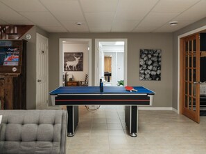 A room with a ping pong table, a grey armchair, and a door leading to another room.