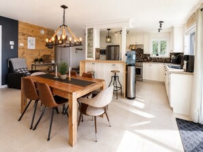 A modern kitchen with white cabinets, a stainless steel refrigerator, and a large island with a sink. - La Baie la Vida,Bord de L`eau,Spa et foyer (Nominingue)