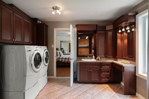 A laundry area with a front-loading washer and dryer, a kitchen with dark wood cabinets and a countertop, and a bedroom visible through an open door.