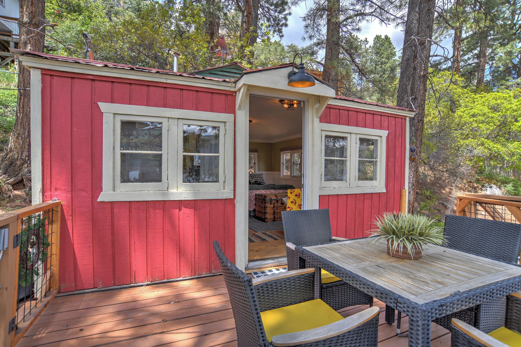 A small red cabin with a porch, wicker furniture, and a view of the surrounding forest.