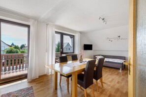 A room with a wooden dining table, chairs, a sofa, a TV, and a balcony with a railing. - Apartment 'Gabis' with Shared Terrace, Shared Garden and Wi-Fi (Munningen)