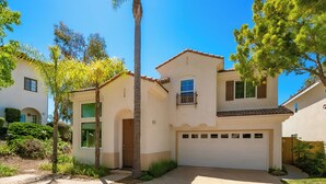 Una casa a due piani con un garage, immersa nel verde e sotto un cielo azzurro intenso.