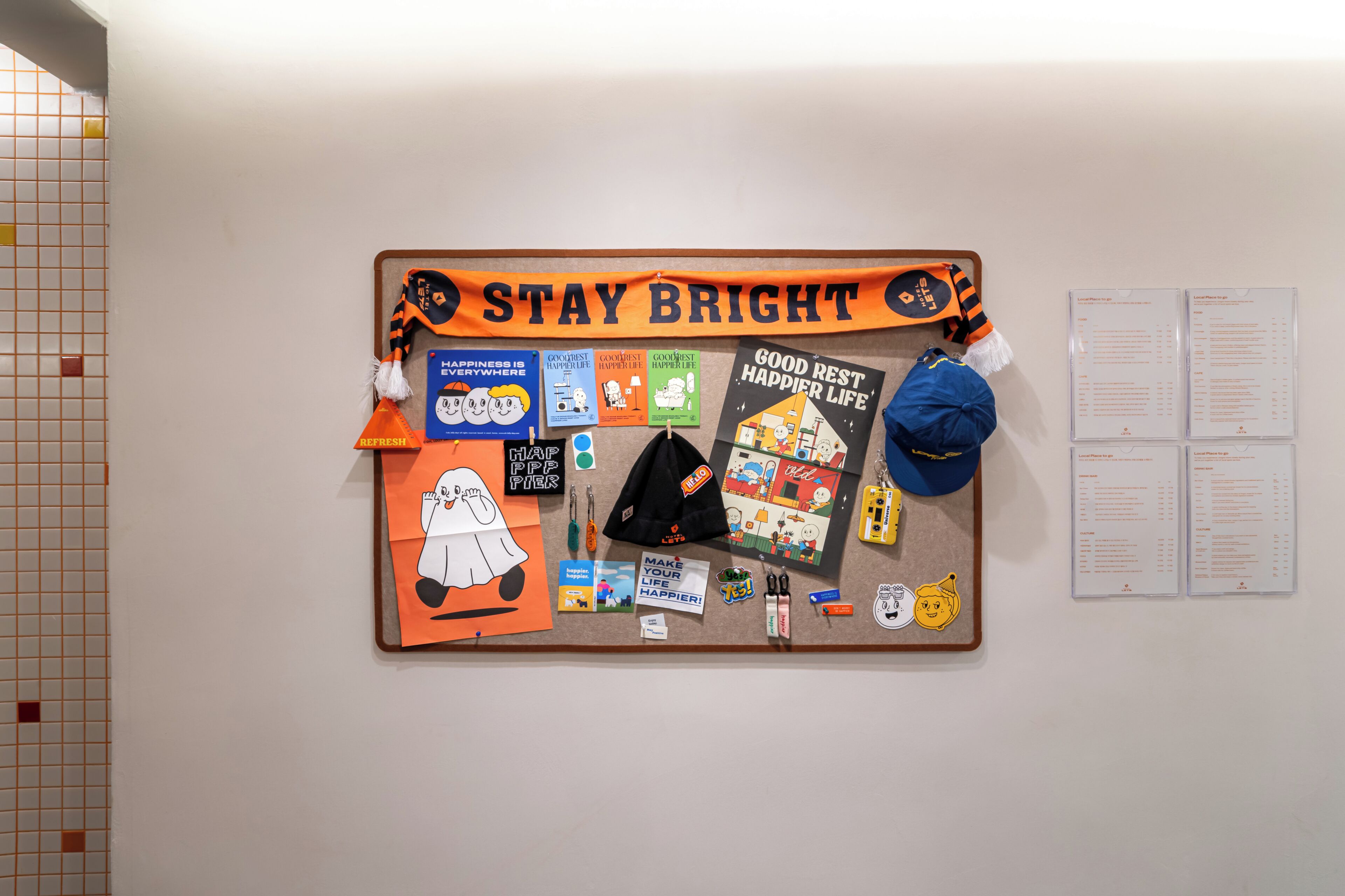 Un tablón de anuncios con carteles motivacionales, un letrero que dice 'Stay Bright' y varios objetos pequeños como un sombrero y un llavero.