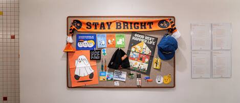 Un tablón de anuncios con carteles motivacionales, un letrero que dice 'Stay Bright' y varios objetos pequeños como un sombrero y un llavero.