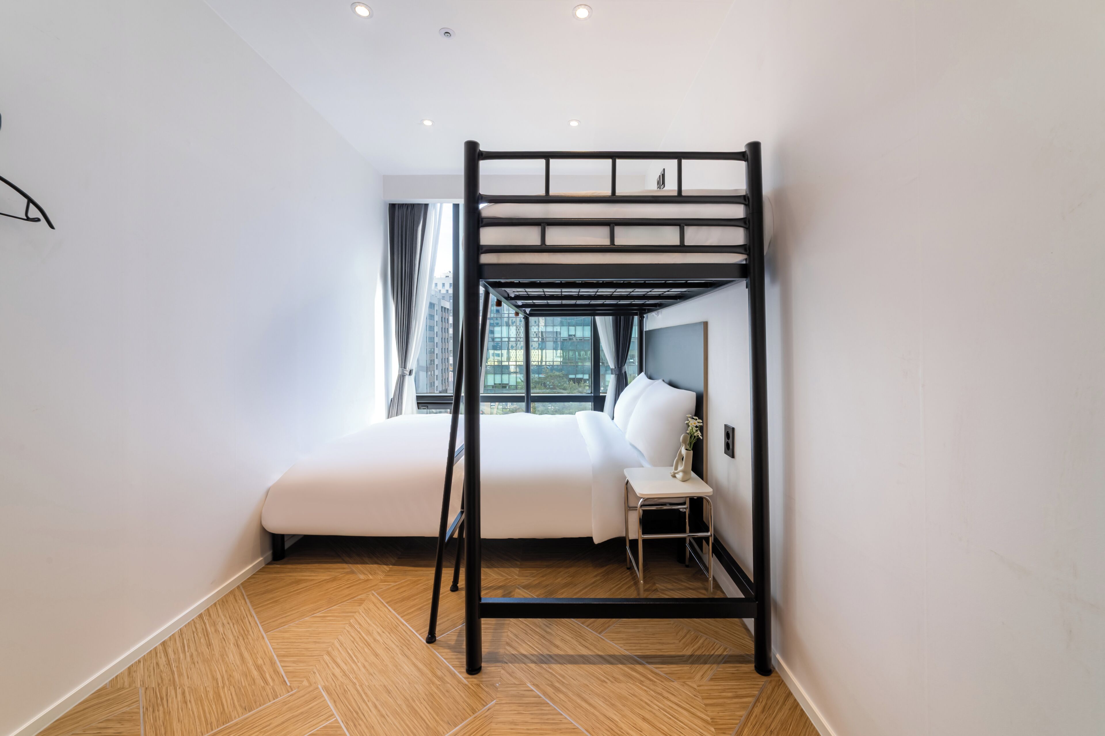 A bunk bed with a desk and chair, a window with curtains, and a city view.