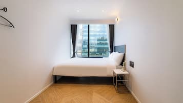 A hotel room with a large bed, a nightstand, a window with curtains, and a view of a cityscape.