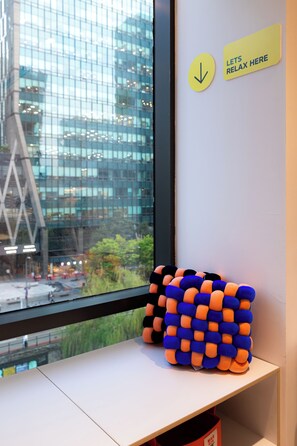 A window with a view of a cityscape, a sign that says 'LET'S RELAX HERE', and a stack of colorful cushions on a shelf. - HOTEL LETS Pop (Seoul)