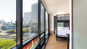 Ein modernes Hotelzimmer mit großem Fenster, einem Bett, einem kleinen Nachttisch und Blick auf die Stadt.