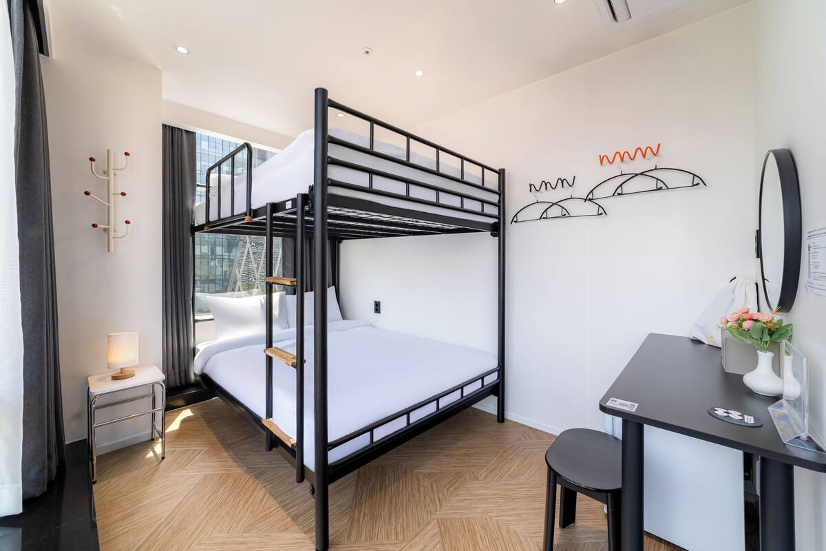 A bunk bed with a desk and chair, a small table with a lamp, and a wall-mounted coat rack.