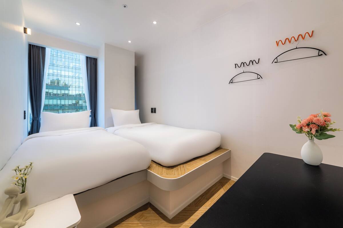 A modern hotel room with a large bed, a small table, and a view of a building through the window.