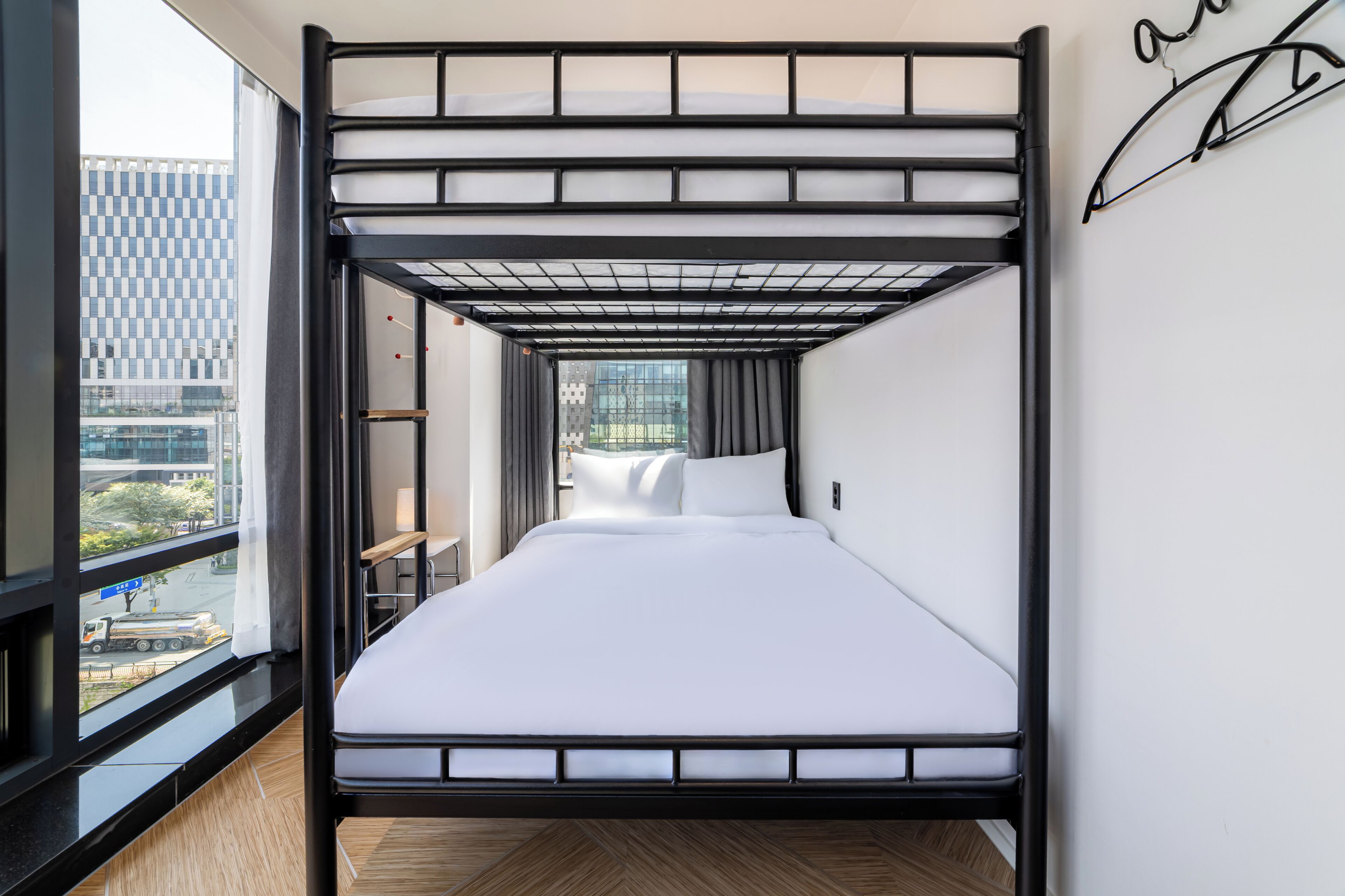 Una cama individual superpuesta con vistas a la ciudad a través de un ventanal grande.