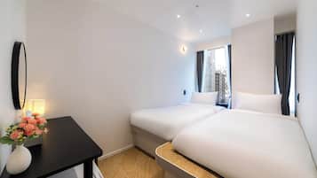Habitación de hotel con dos camas, un escritorio con un florero y una ventana con cortinas.
