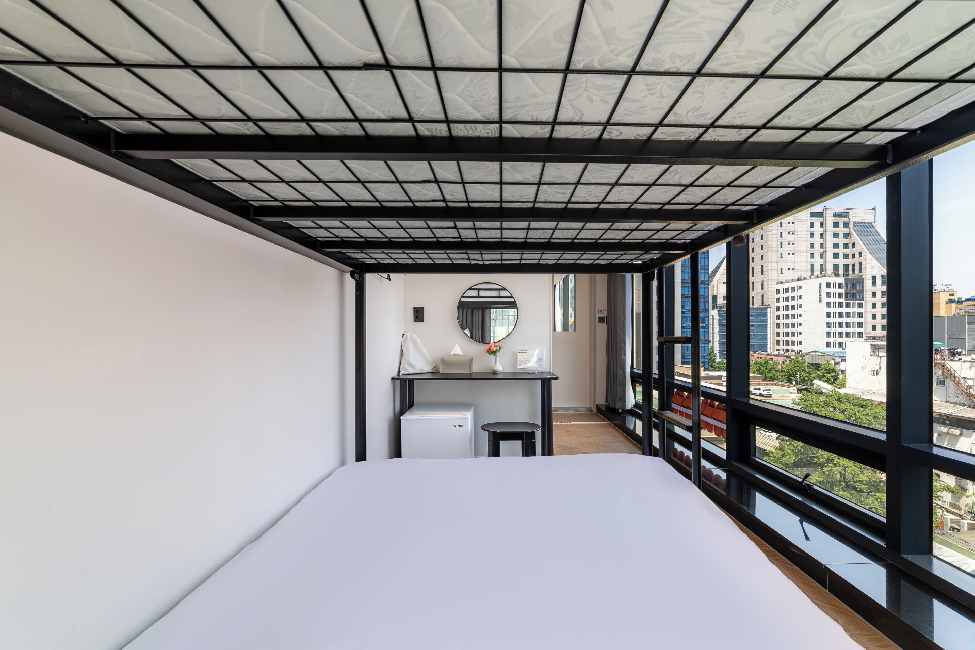 A modern hotel room with a large bed, a desk, and a view of the city.