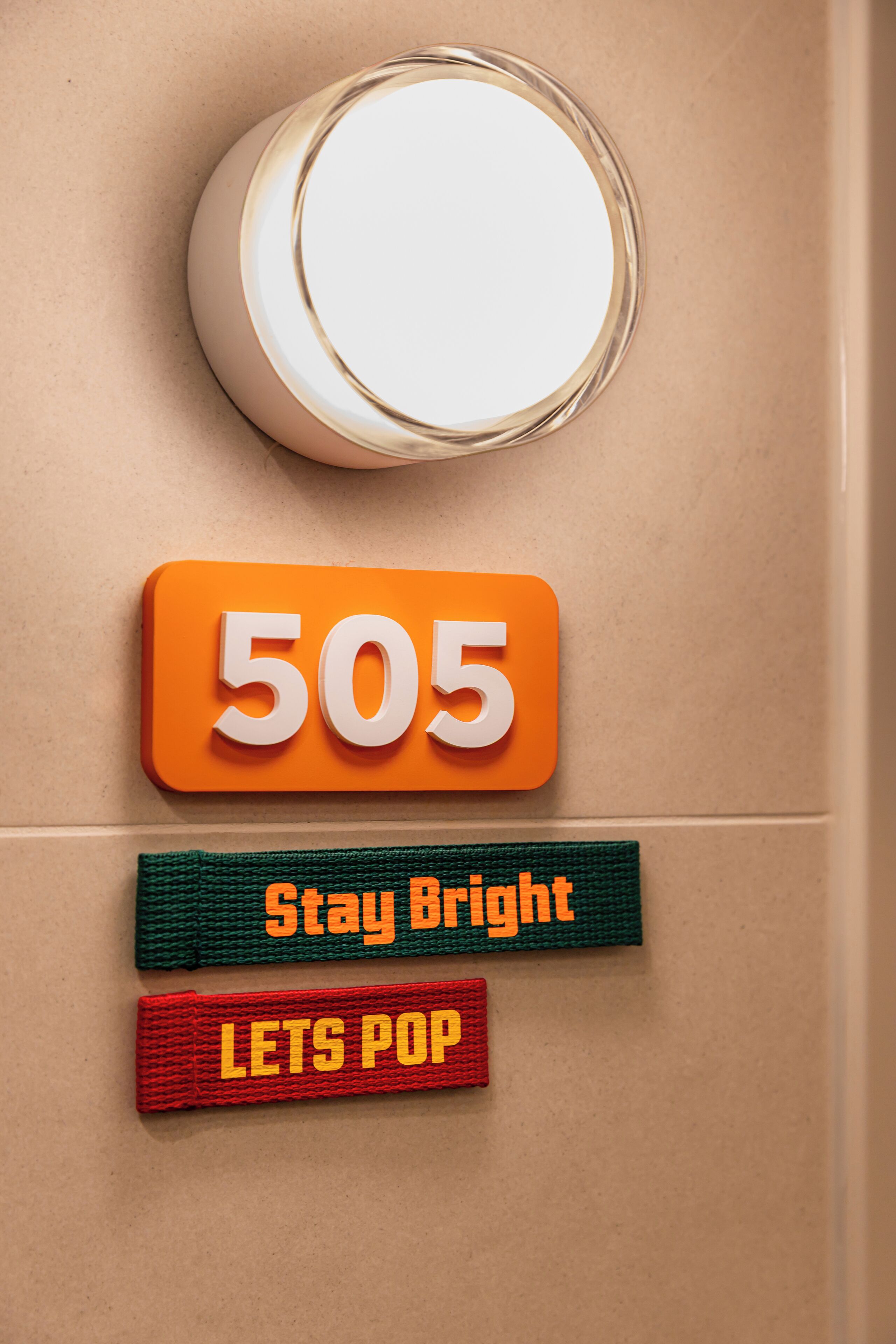 Een muur met een ronde spiegel, een bord met het nummer 505, en twee motiverende banners met de tekst 'Stay Bright' en 'Lets Pop'.