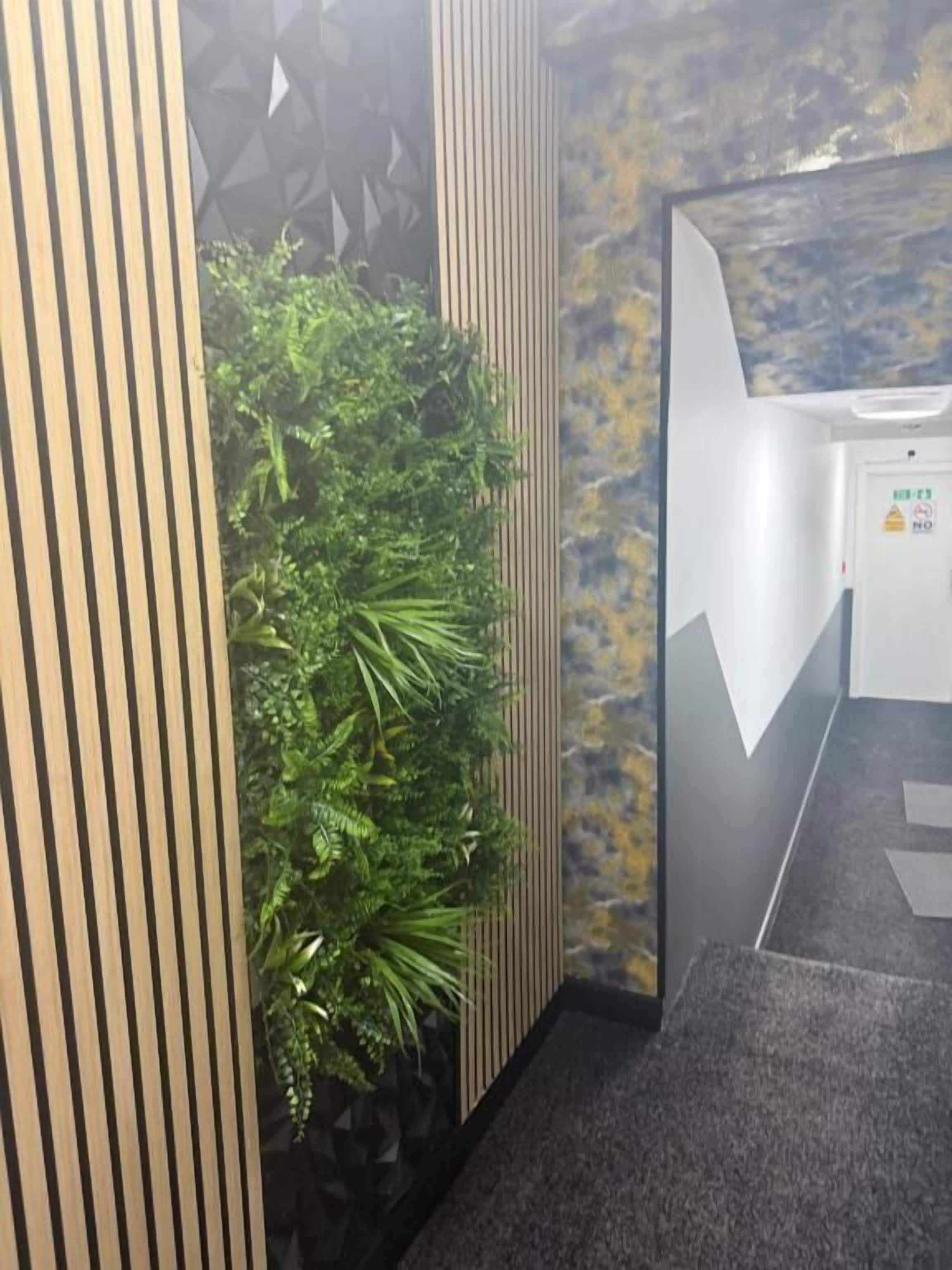 Un baño con un panel vertical, una planta en la pared y un lavamanos con un letrero de advertencia.