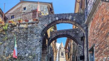 Una calle estrecha con edificios de piedra, una torre de iglesia a lo lejos y una bandera colgada a la izquierda.