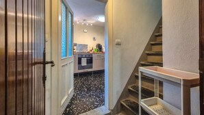 A hallway leading to a kitchen with a black and white speckled floor, a staircase, and a white door with vertical lines. - The Tinello - Virgoletta (Virgoletta)
