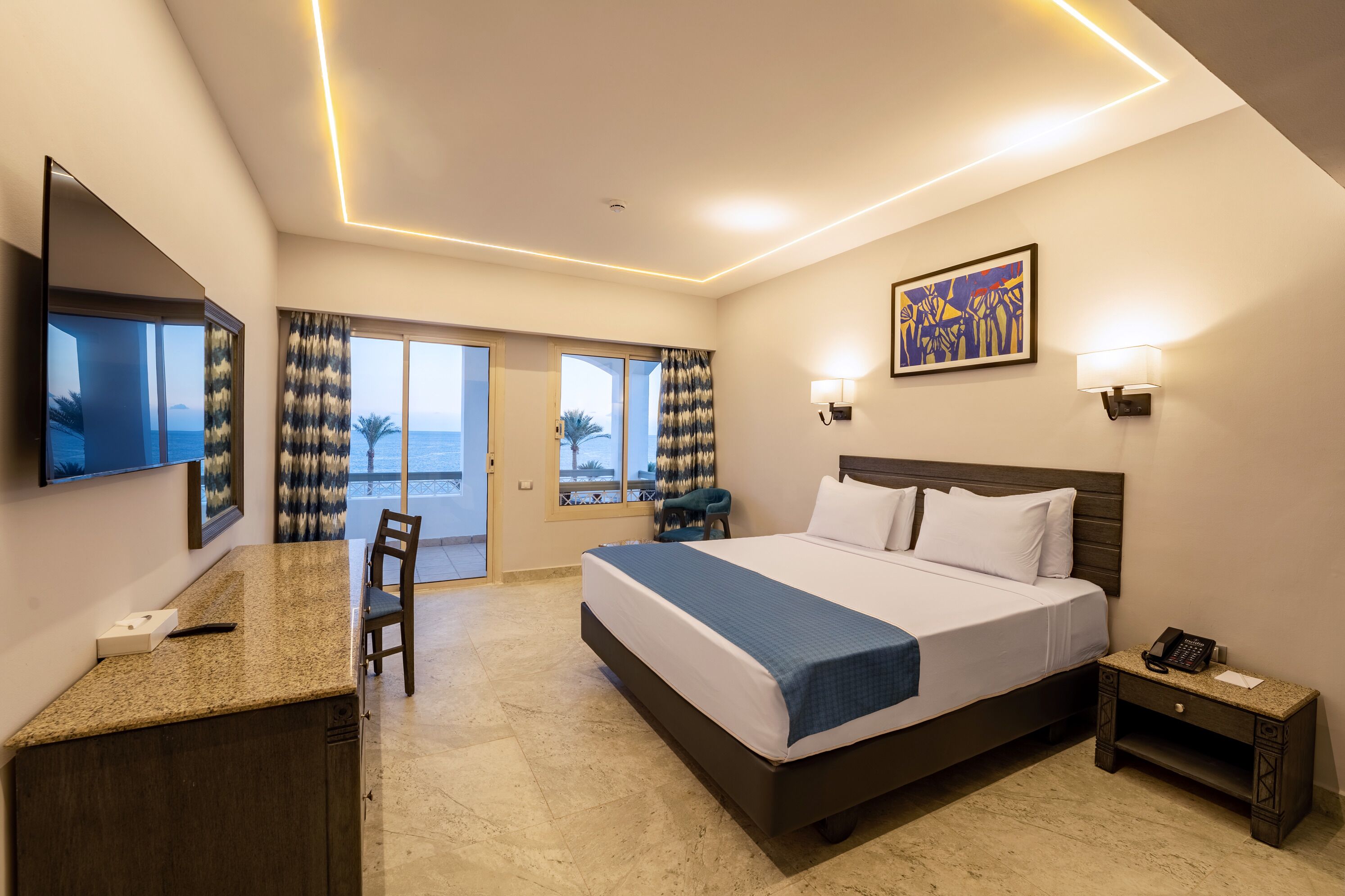 A hotel room with a bed, desk, chair, and a view to the outside.