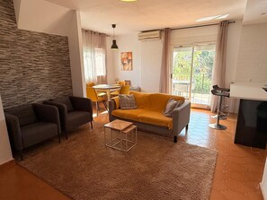 Ein Wohnzimmer mit einer Couch, Sesseln, einem Couchtisch und einem Essbereich mit Tisch und Stühlen.