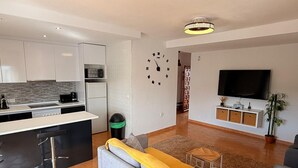 Um espaço de estar moderno com cozinha, sofá, televisão e um relógio decorativo na parede.