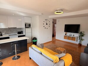 Ein stilvolles Wohnzimmer mit Küche, Sofa, Fernseher und einer Wanduhr.