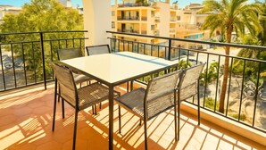 Uma varanda com mesa e cadeiras, vista para edifícios e uma palmeira.