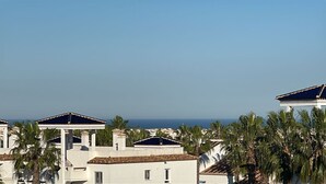 Uma área residencial costeira com edifícios brancos, alguns com telhados azulejados em azul, e palmeiras.