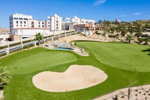 Ein Golfplatz mit einem großen Bunker, einer Wasserfalle und einem Gebäude mit weißer Fassade und Rundbogenfenstern.