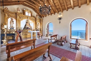 Ein Kircheninneres mit Holzbänken, einem goldenen Altar und Blick auf das Meer durch große Fenster.