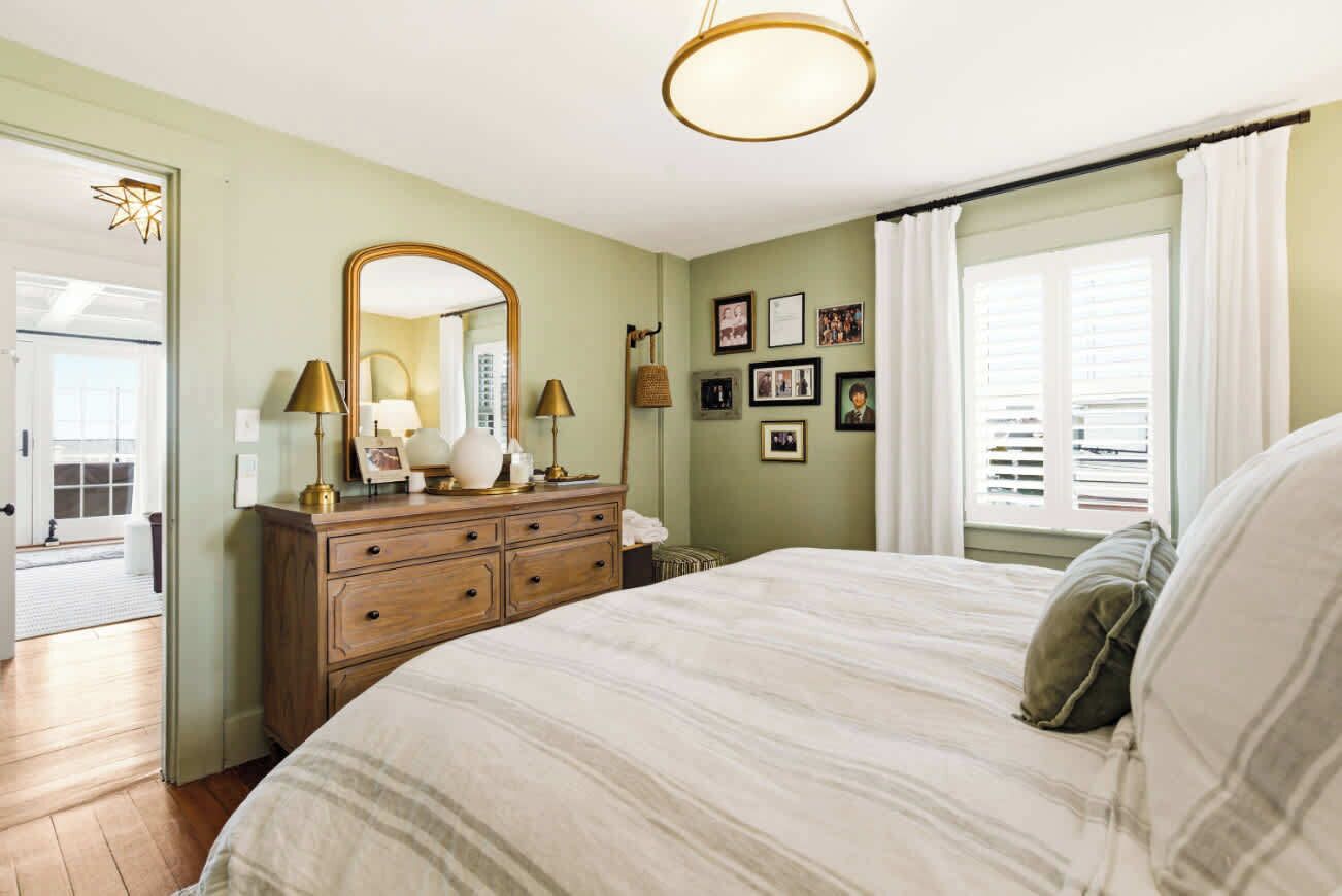 A bedroom with a bed, dresser, mirror, and wall-mounted lamps.