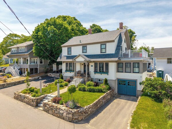 A two-story house with a front porch, a stone retaining wall, and a small garden. - Casa sul Mare Near the Coast (Ogunquit)