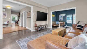 A spacious living room with a large flat-screen TV, a leather sofa, a wooden coffee table, and a patterned rug. - Walk to Beach | Parking | Sleeps 10 (Asbury Park)