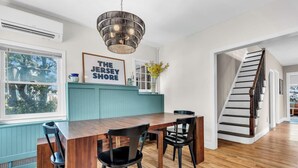 A dining area with a wooden table and chairs, a pendant light, a framed sign, a window with a view, and a staircase. - Walk to Beach | Parking | Sleeps 10 (Asbury Park)