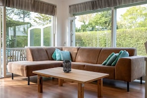Un salon moderne avec un canapé marron, une table basse en bois et de grandes fenêtres donnant sur un paysage verdoyant.