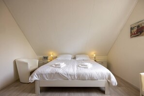 Une chambre à coucher comprenant un lit, deux tables de chevet, une commode, une chaise et un tableau accroché au mur.