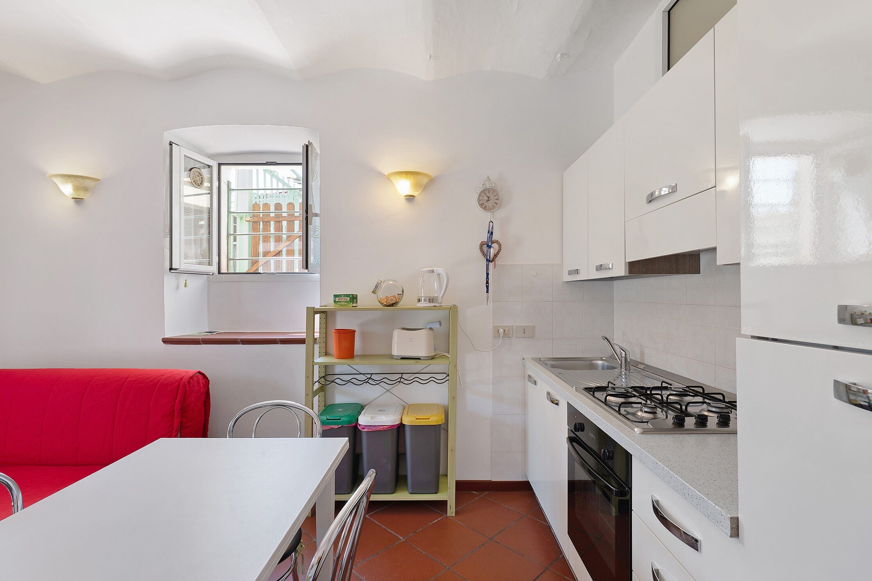 Una cucina funzionale con mobili bianchi, un divano rosso e una finestra vista edificio.