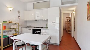 A compact kitchen with white cabinets, a white table, and chairs, a stove, and a refrigerator.