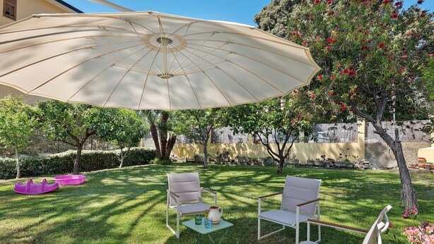 A patio with a large umbrella, two chairs, a small table, and a tree with red flowers.