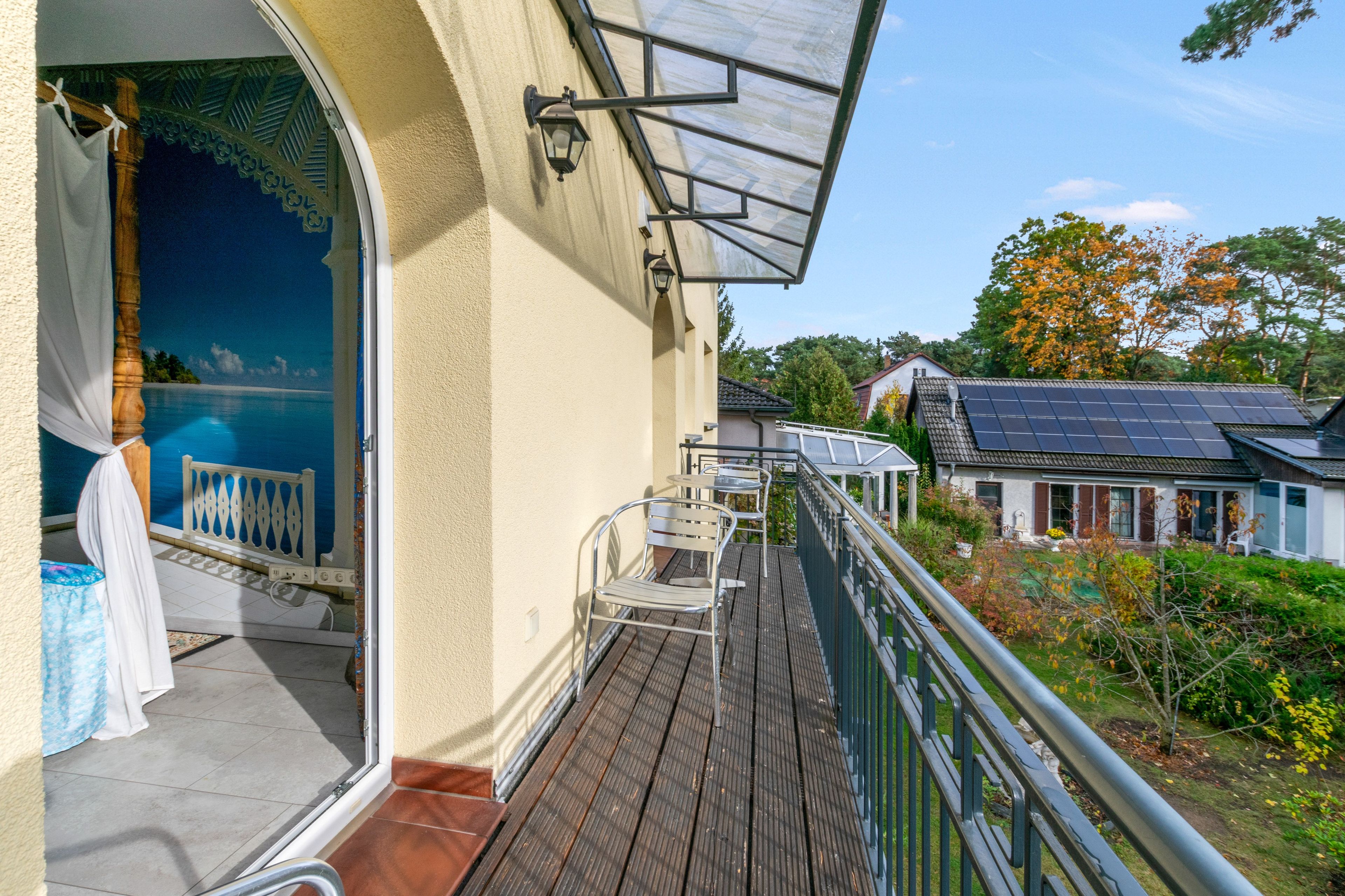 A balcony with a view of a swimming pool, a solar panel, and a neighboring house.