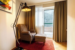 A room with a chair, ottoman, floor lamp, and a view of a balcony with curtains. - Garden suite vacation apartment with pool in Saalbach-Hinterglemm (Hinterglemm)
