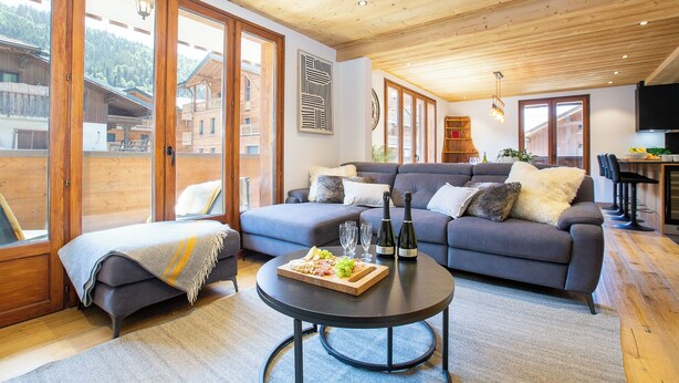Een woonkamer met een bank, een bijzettafeltje met eten en een fles wijn.