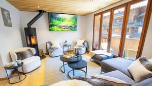 Een gezellige woonkamer met een open haard, comfortabele zithoek, een televisie en uitzicht naar buiten.