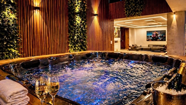 Ein Whirlpool mit zwei Weingläsern und einer Champagnerflasche, umgeben von Holzverkleidungen und Innenbeleuchtung.