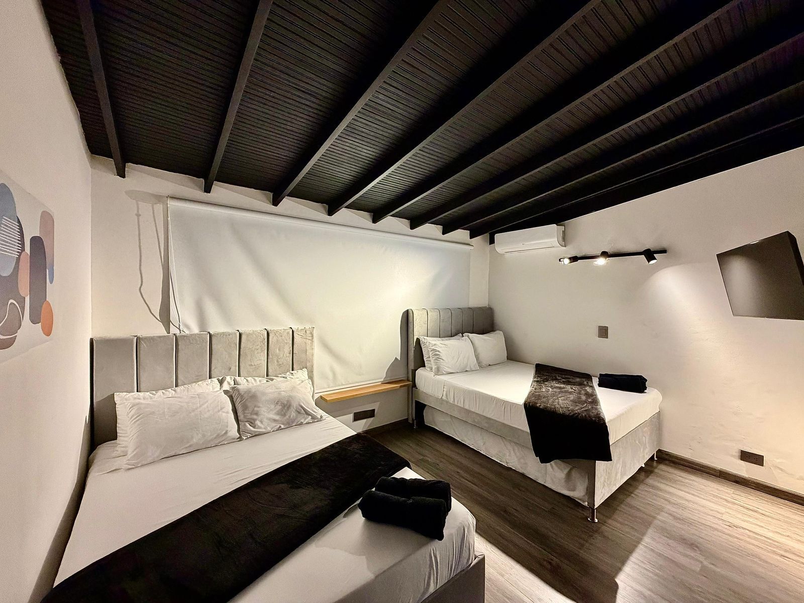 A modern room with two beds, a wooden ceiling, and a white wall.