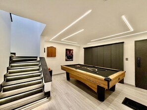 A modern room with a pool table, a staircase, and a door.