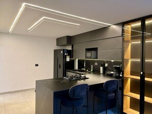 A modern kitchen with a central island, bar stools, a microwave, and a coffee machine.