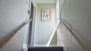 Eine Treppe mit Teppichstufen, Holzhandläufen und einem Bilderrahmen mit dem Schriftzug 'HOME' an der Wand.