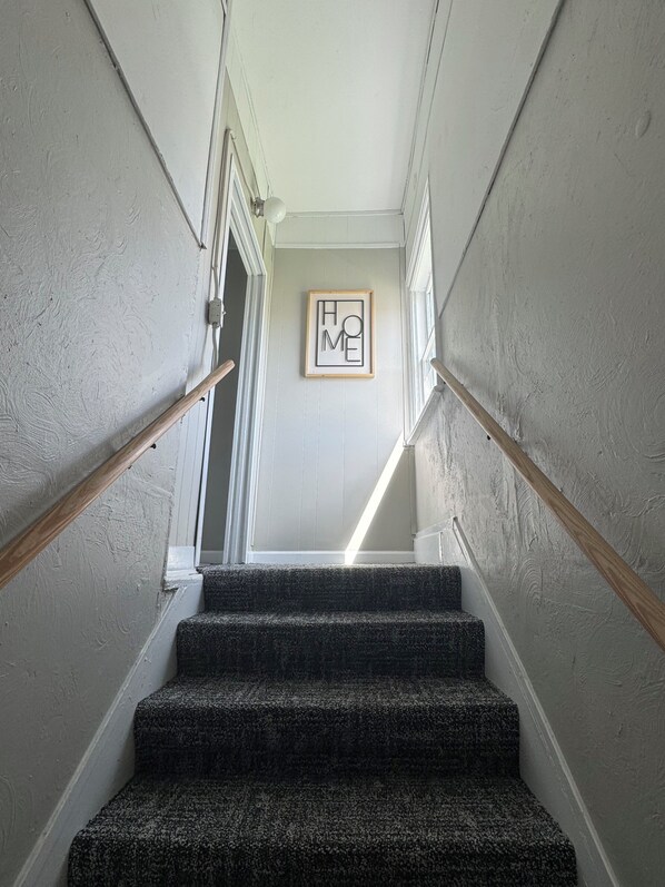 A staircase with carpeted steps, wooden handrails, and a framed 'HOME' sign on the wall.