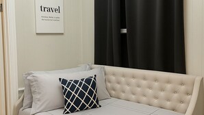 Ein beiges Sofa mit einem Kissen mit Rautenmuster, ein gerahmtes Schild an der Wand und schwarze Vorhänge.